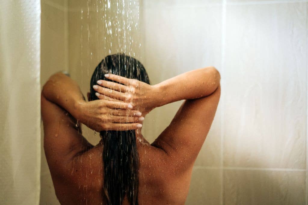 Woman with long hair in the shower, hands on head, water falling.
