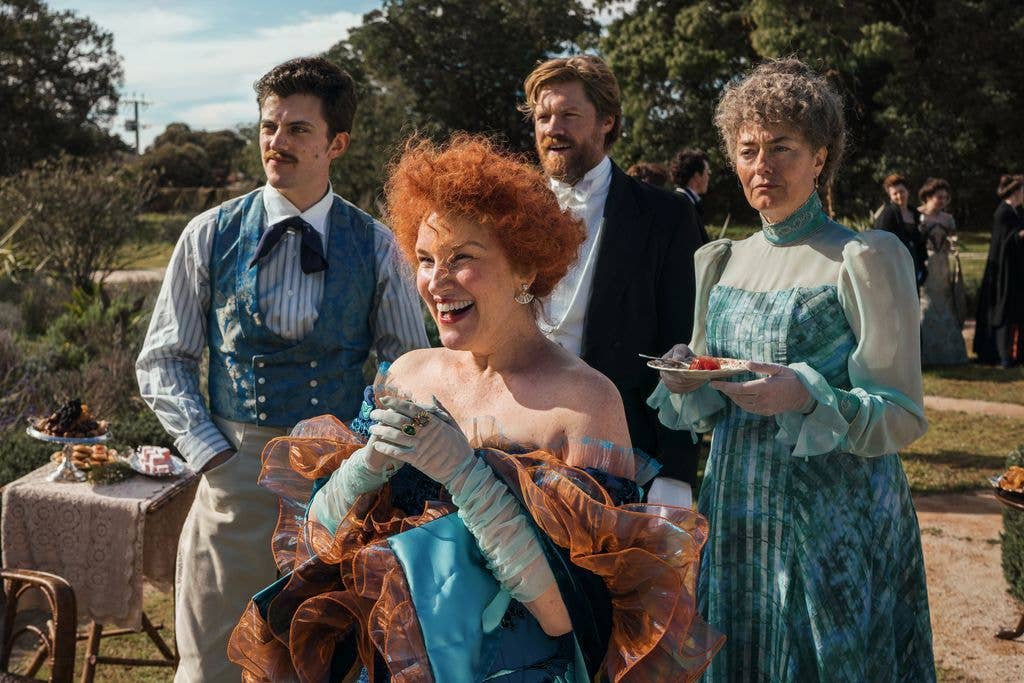 Anna Chancellor stands with three others in period attire, holding a plate, smiling.