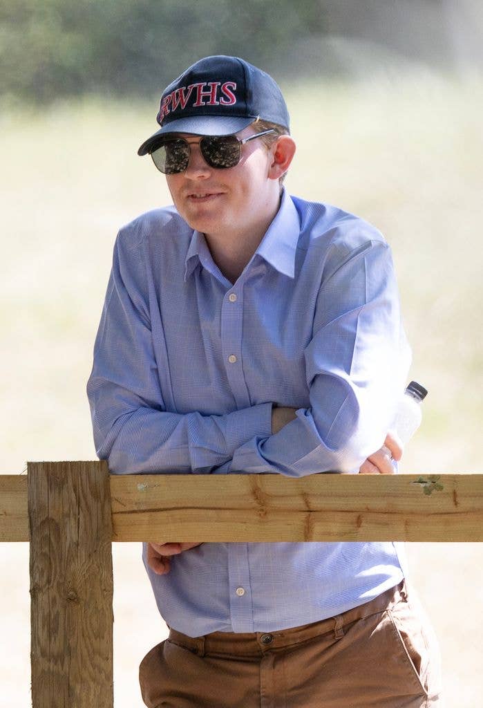 Man in blue shirt and RWHS cap leaning on a fence, smiling.