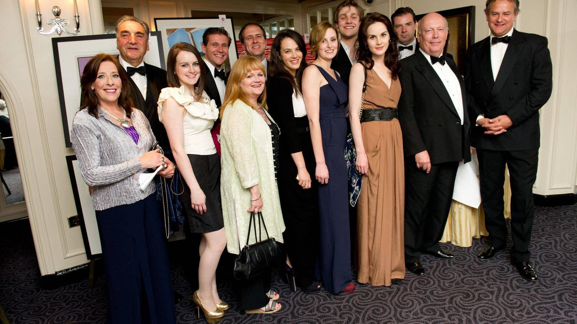 Group photo of Julian Fellowes and other individuals in formal attire, smiling and posing together.