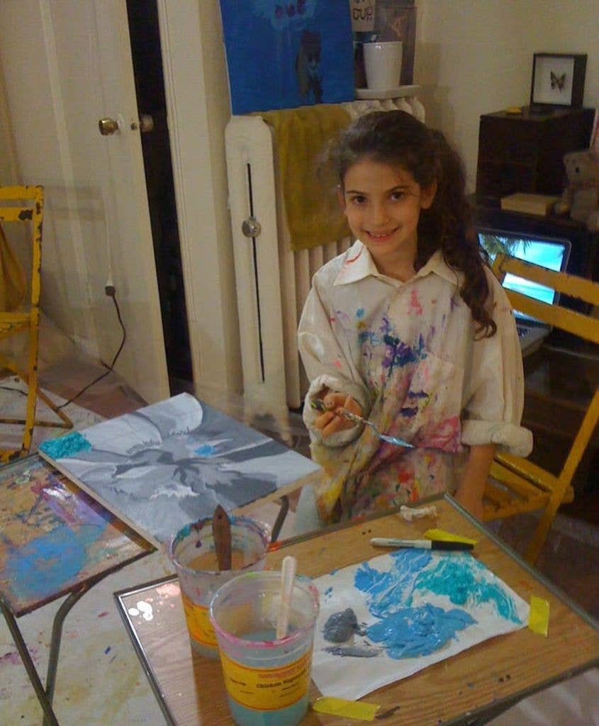 Ella Rubin as a child holding a paintbrush, wearing a paint-splattered shirt
