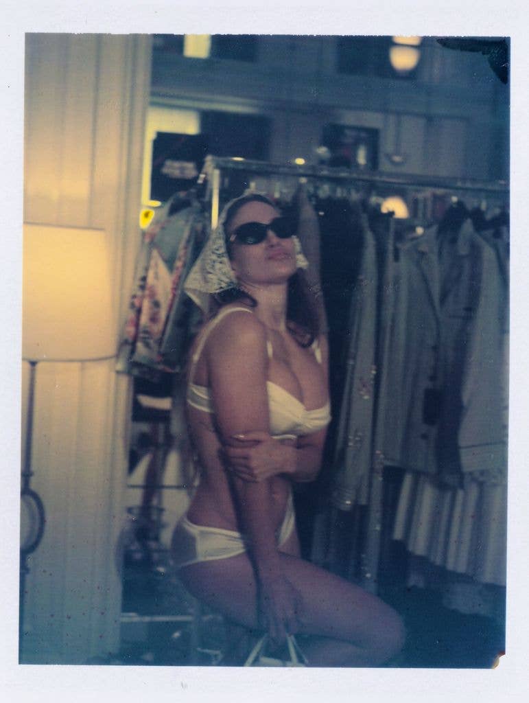 Jennifer Lopez wearing white bra and matching underwear, sunglasses, and a headscarf, posing in front of clothing rail
