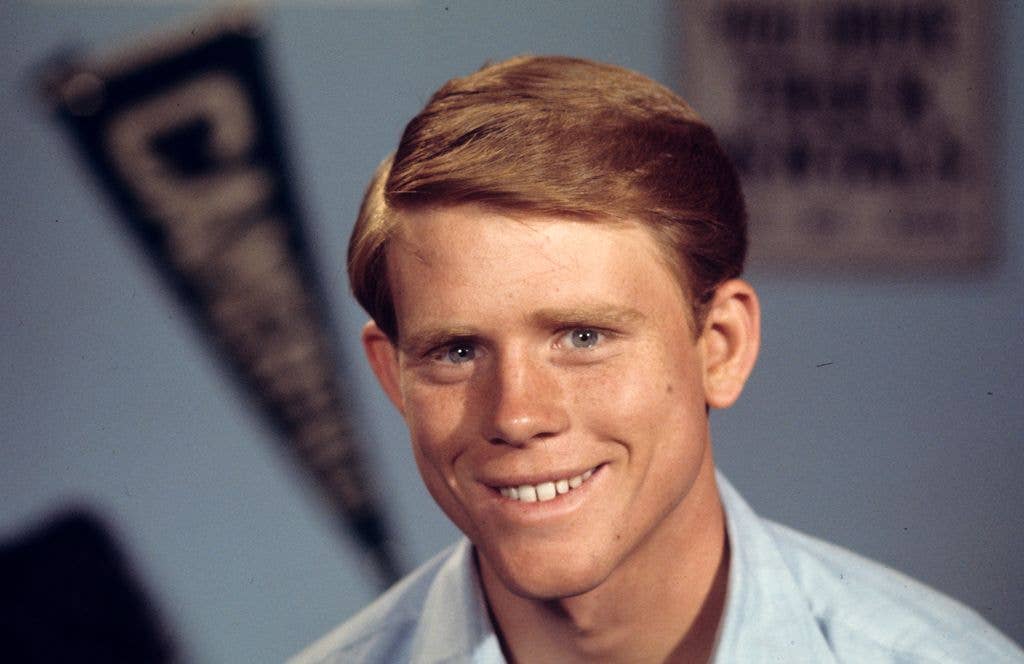 Young Ron Howard smiling in a light blue shirt against a blue background.