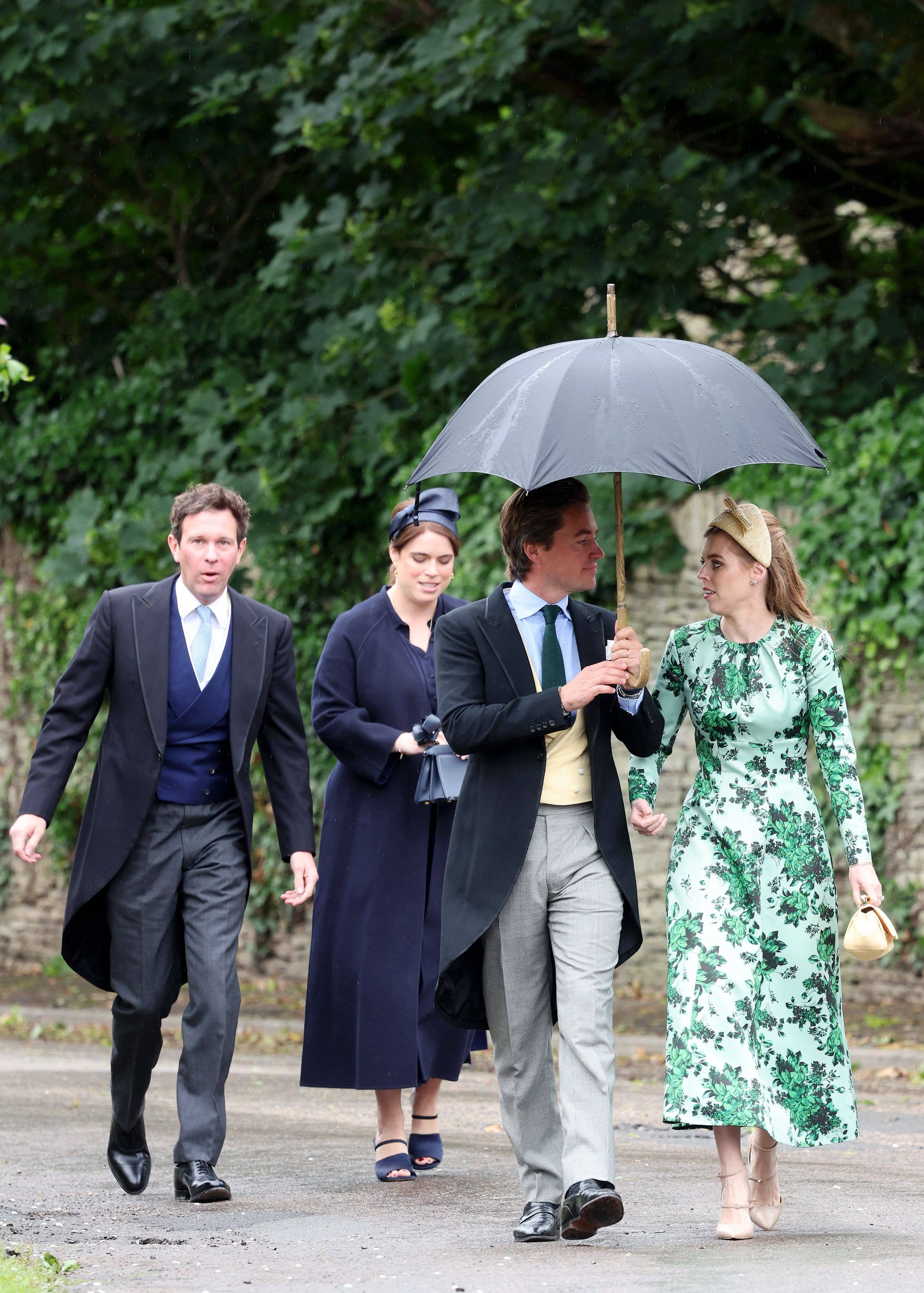 Four people walking on a path with one holding an umbrella. No celebrities detected.