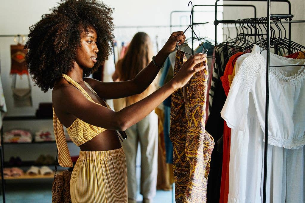 Woman in yellow striped dress browsing clothes on rack in store.