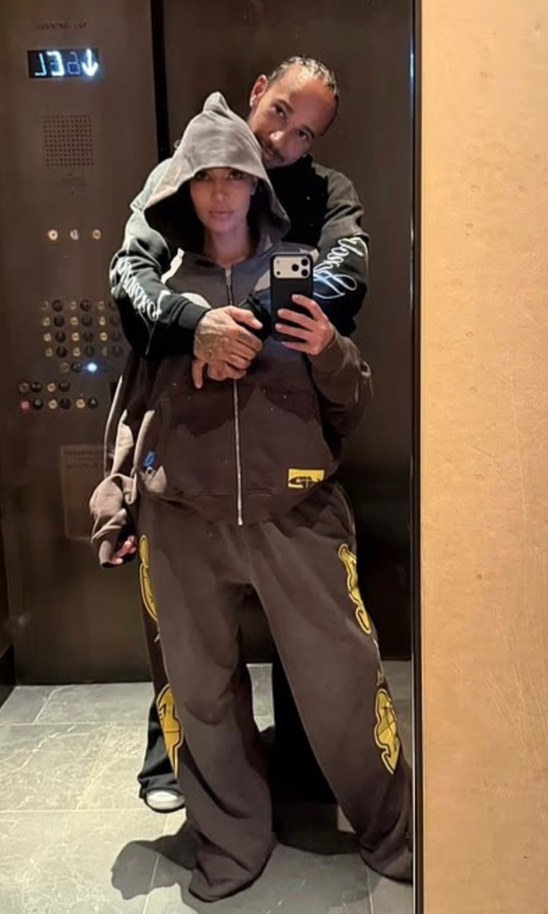 Kim wears an oversized hooded tracksuit while Lewis stands protectively behind her