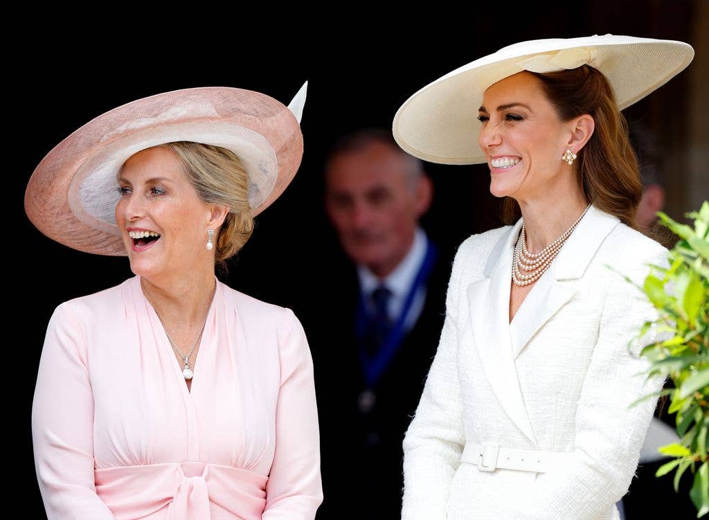 Duchesss Sophie in pink dress and hat, laughs with Kate Middleton in white suit and hat.