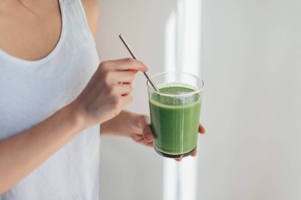 Cropped shot of young woman drinking vegan smoothie with metal straw.