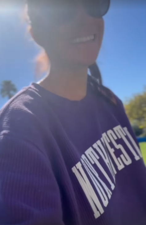 Meghan Markle wearing a purple Northwestern sweater while smiling and walking through her garden