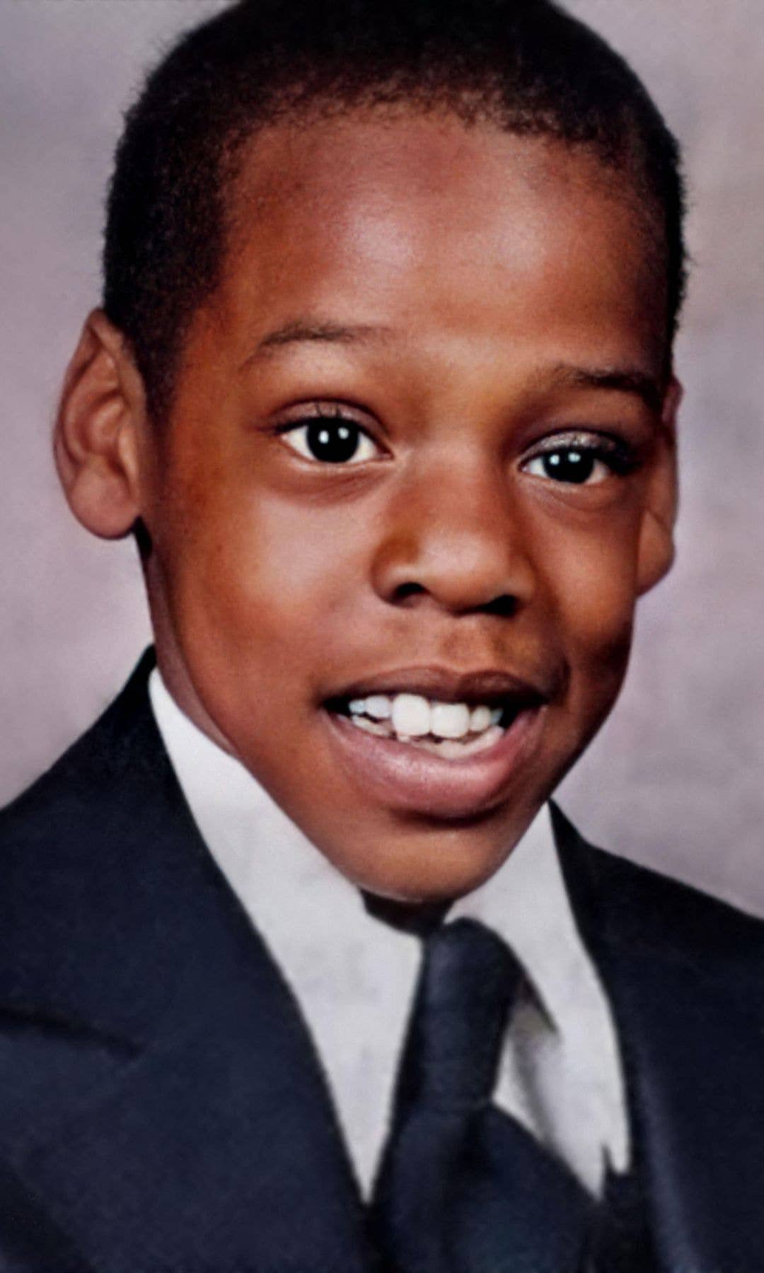 Young boy in a dark suit and tie, smiling brightly at the camera.