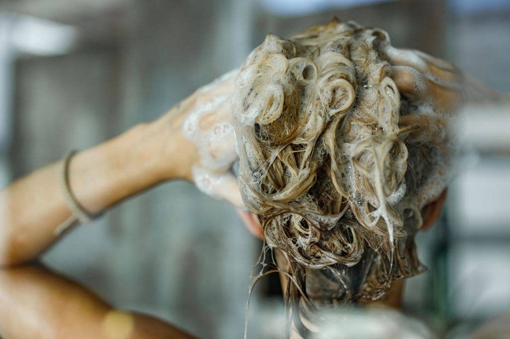 Back view of a woman washing her hair with a shampoo in bathroom 