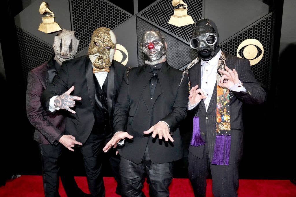 Four masked individuals in formal attire pose together on a red carpet.