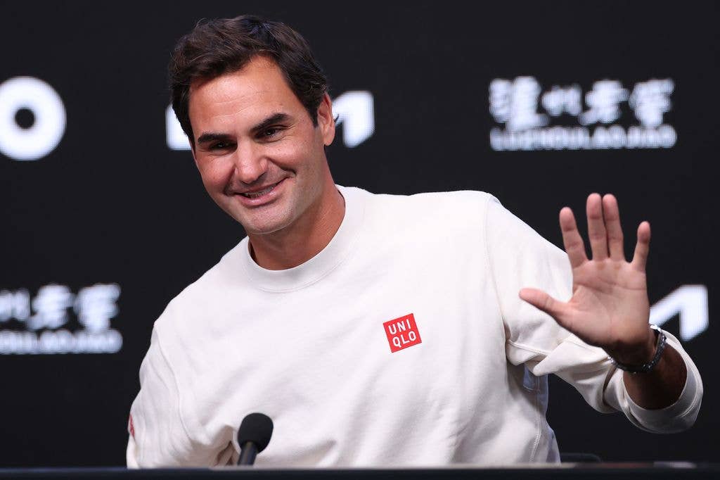 Roger Federer holds up a hand and smiles at a press conference.