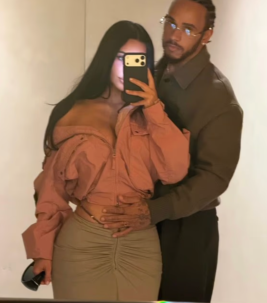 Kim wears an oversized hooded tracksuit while Lewis stands protectively behind her
