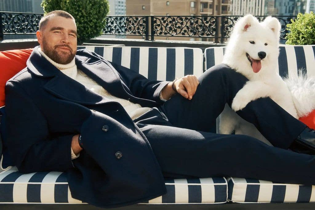 Travis Kelce is lying on a striped couch with his white Samoyed leaning on his knee
