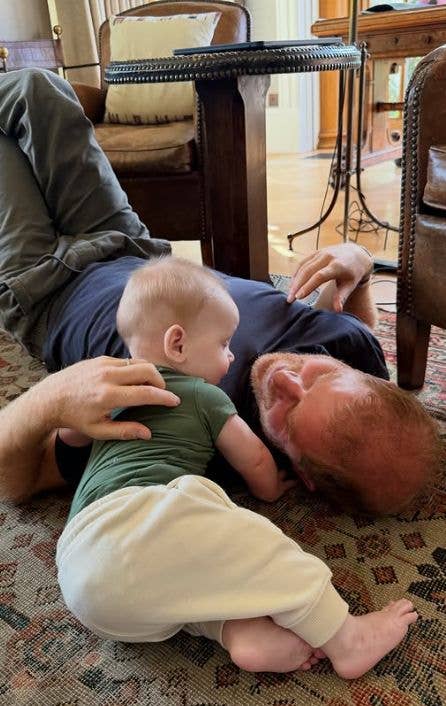 Man lying on rug with baby on his chest, both looking at something.