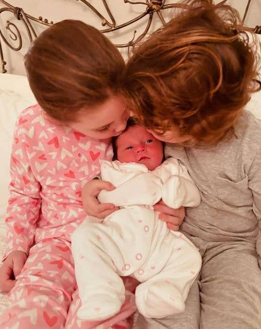 Two young children in pajamas hug a swaddled baby, showing affection.