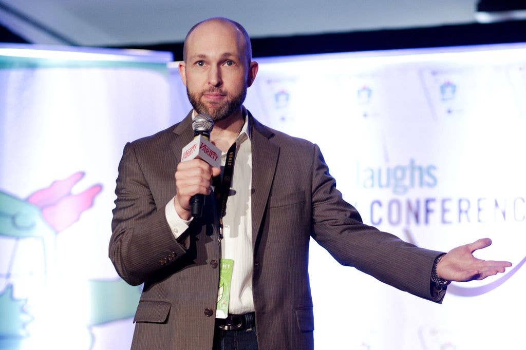 Jeff Cohen holds a microphone and gestures with his left arm.