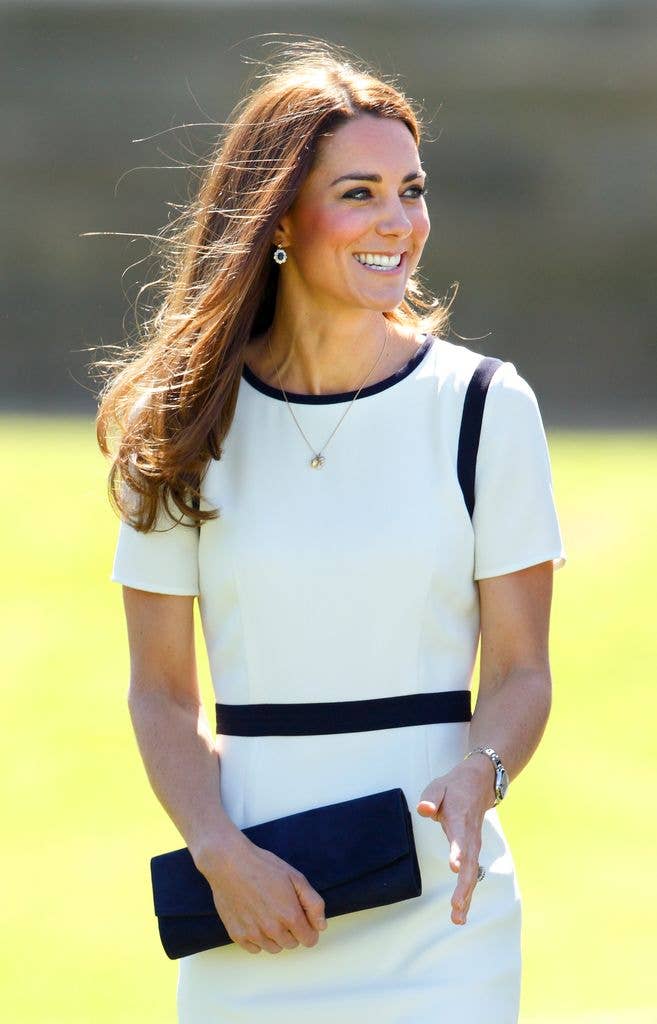 Kate Middleton smiling, wearing a white dress with black trim, holding a blue clutch.