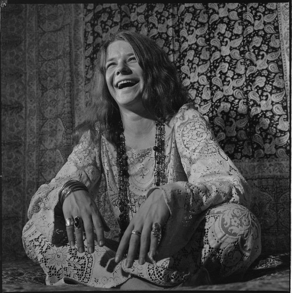 Janis Joplin, laughing, sitting on a bed