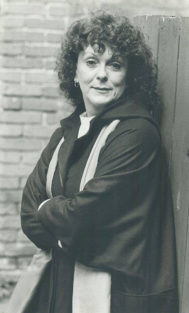 Black and white portrait of Shirley Jean Douglas with curly hair, arms folded, leaning against a wooden fence.