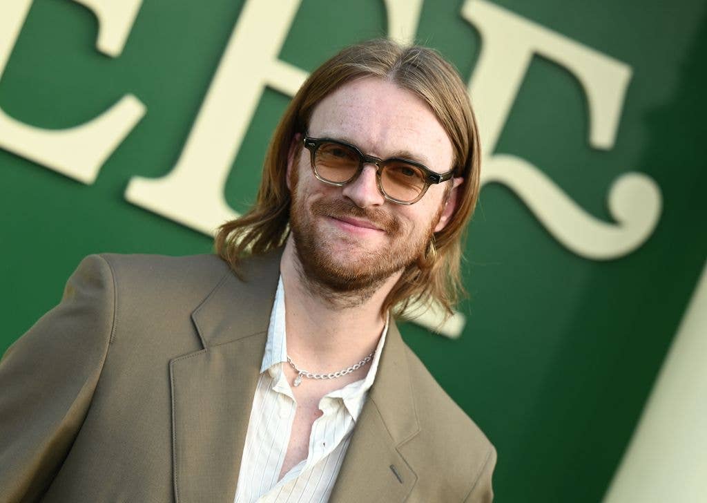 Man with long hair and beard wearing glasses and a suit, smiling at the camera.