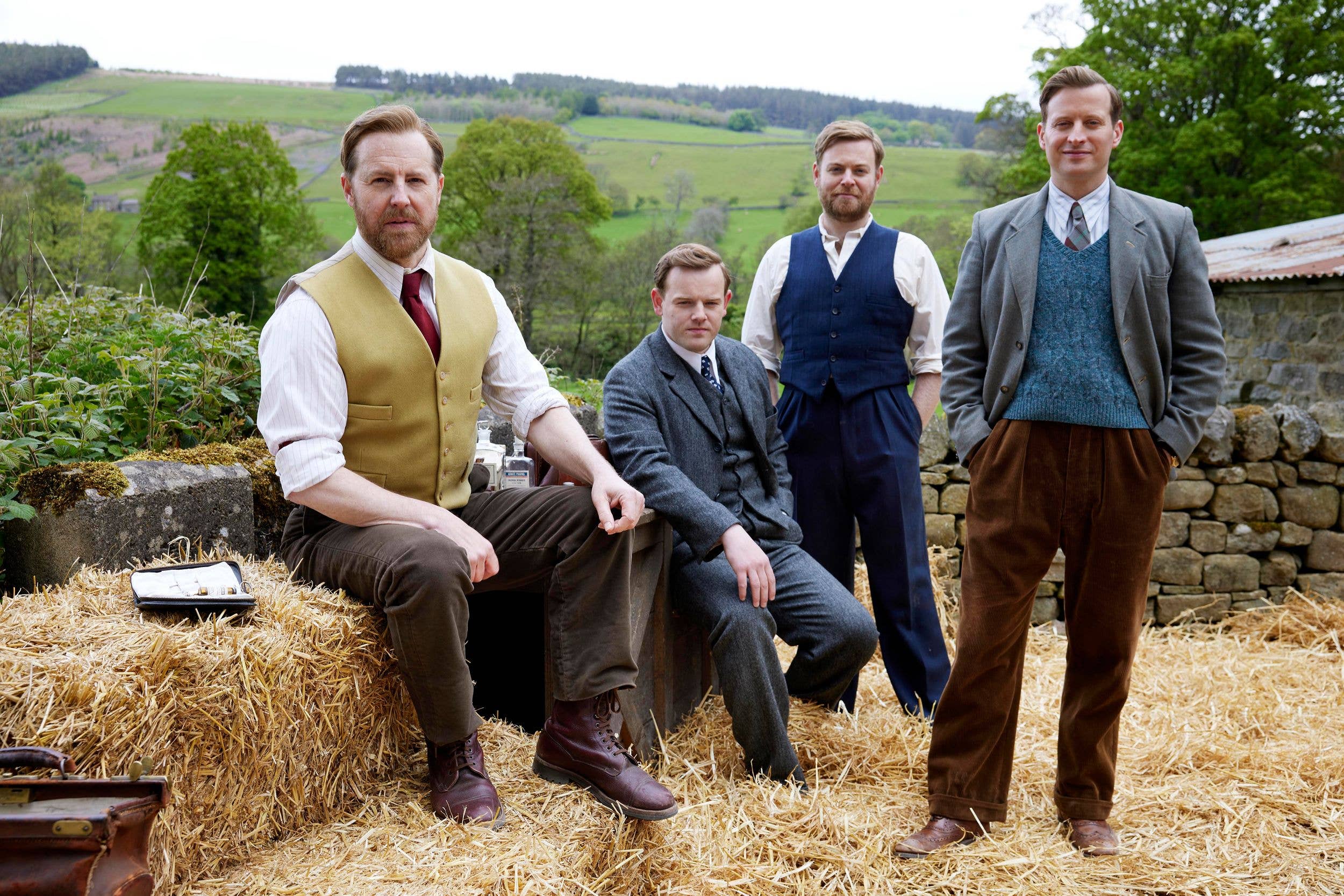 Samuel West, seated on hay bale, with three men in suits and vests, in a rural setting.