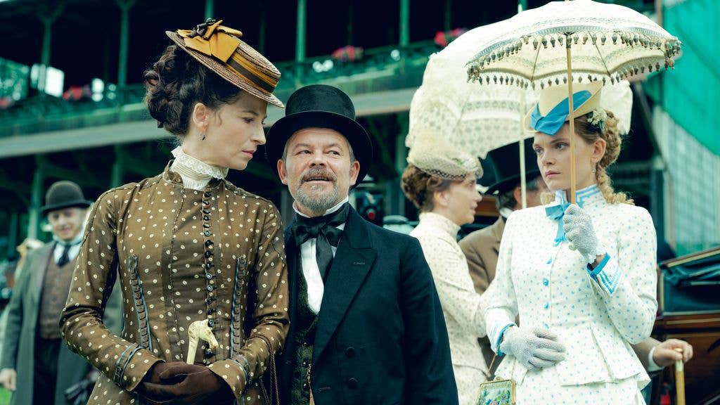 Jacek Braciak in a black suit and top hat stands between two women in period attire.