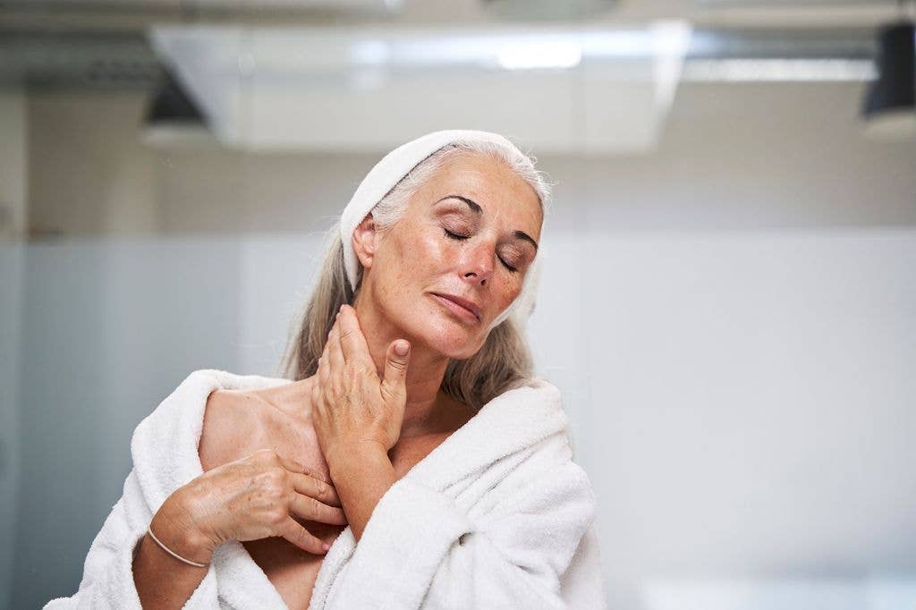 Woman with eyes closed massaging neck in bathroom