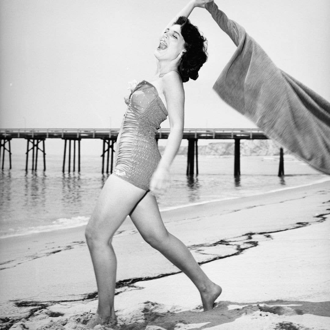 A portrait of actress Anne Bancroft swinging a towel on a beach circa 1950's.