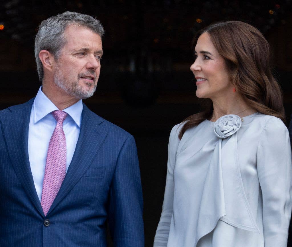Queen Mary of Denmark stands next to a man in a blue suit, both smiling.