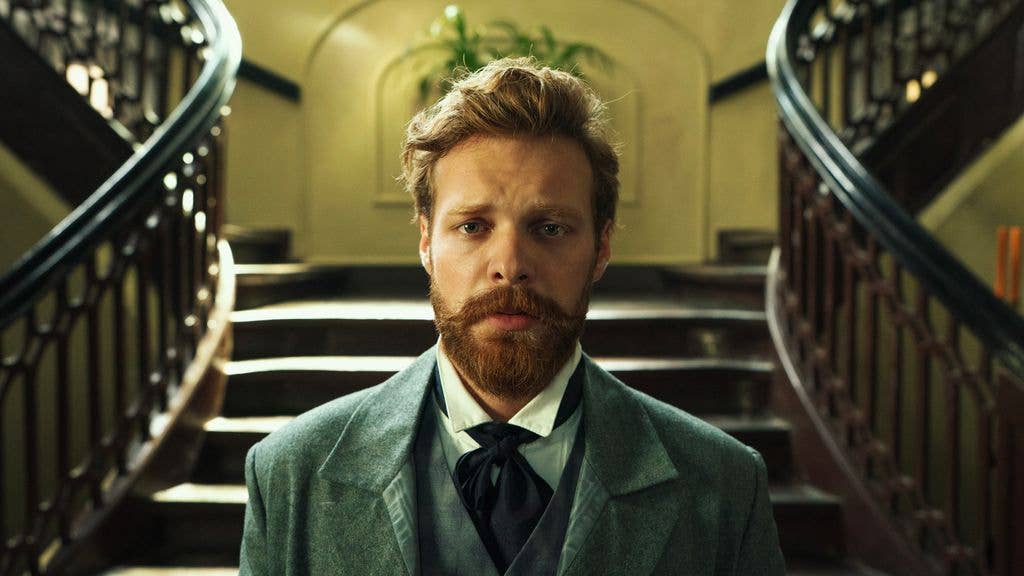 Man with a beard in a suit and bow tie stands on a staircase.