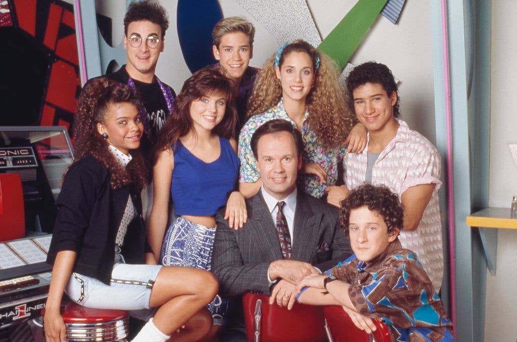 Group photo of 'Saved by the Bell' cast with Dennis Haskins seated, Lark Voorhies, Tiffani Thiessen, Elizabeth Berkley, Mario Lopez, and Mark-Paul Gosselaar standing.