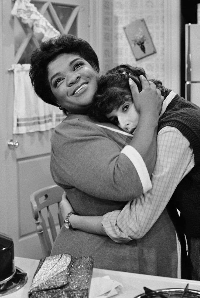 A black-and-white photo of Nell Carter, smiling, warmly hugging Lara Jill Miller in a kitchen set from the sitcom Gimme a Break.