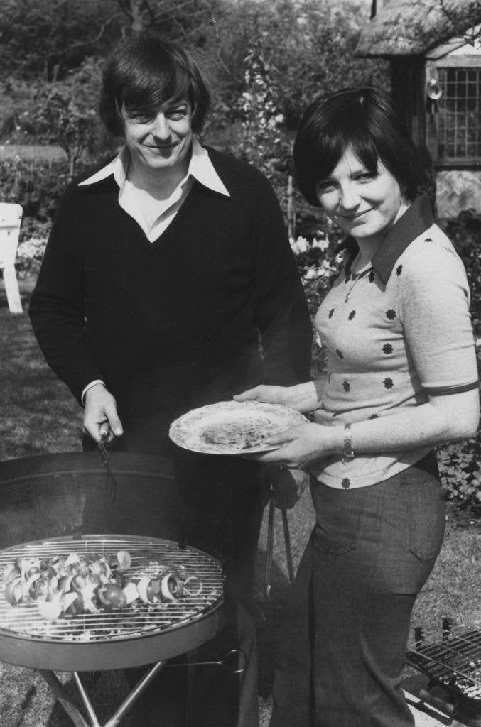 Delia Smith and a man grilling food on a barbecue, smiling.