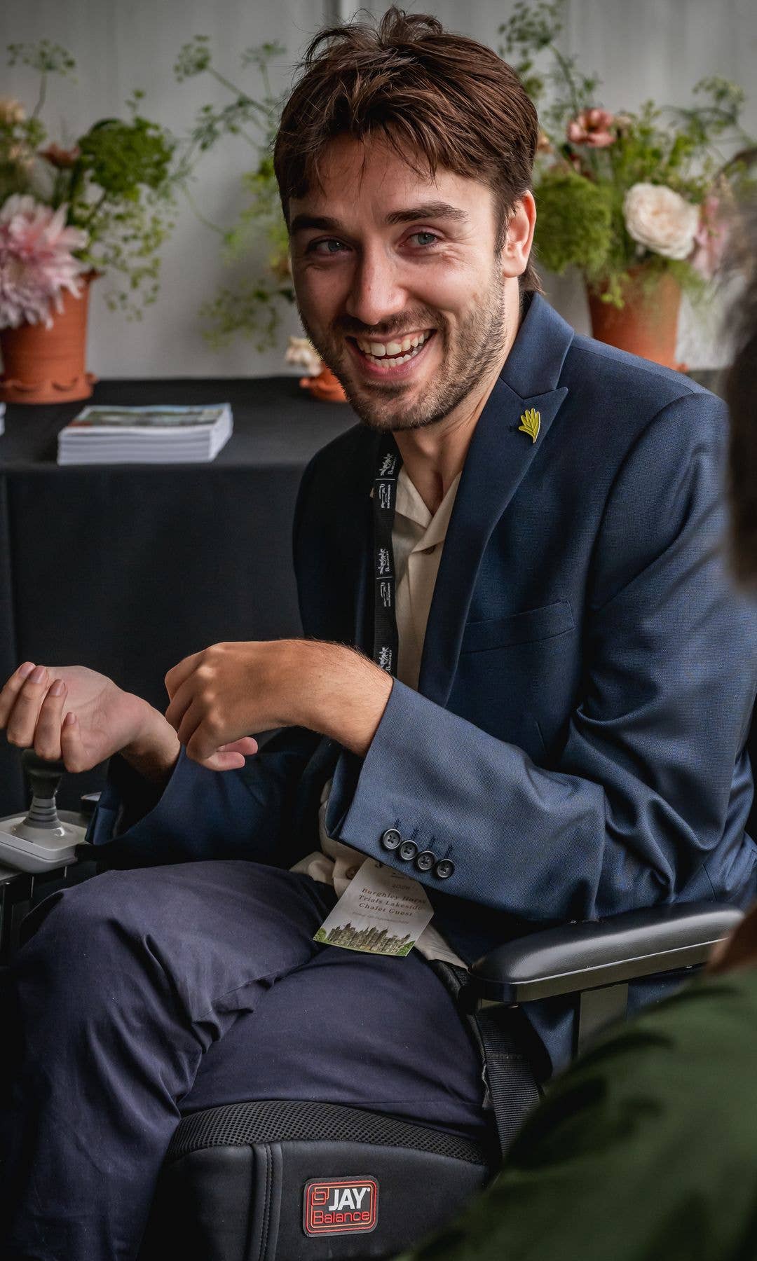George Robinson in a blue suit and white shirt, smiling and sitting in a chair with a name tag.