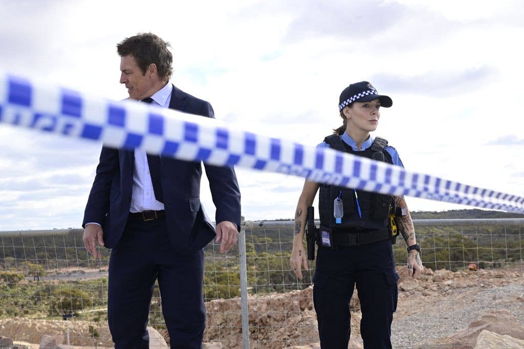Steve Peacocke in a suit and Sheridan Smith in police uniform stand by a crime scene tape.