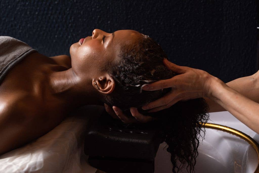 Woman receiving a hair wash and scalp massage at a salon.