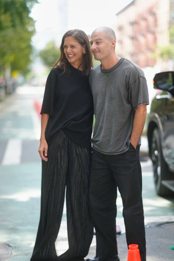 Katie Holmes is seen wearing gold hoop earrings, black short-sleeve top, black pleated wide-leg trousers, black shoes, Jason Bard Yarmosky is seen wearing a grey t-shirt and black trousers during New York Fashion Week Spring Summer 2027 on September 09, 2026 in New York City.
