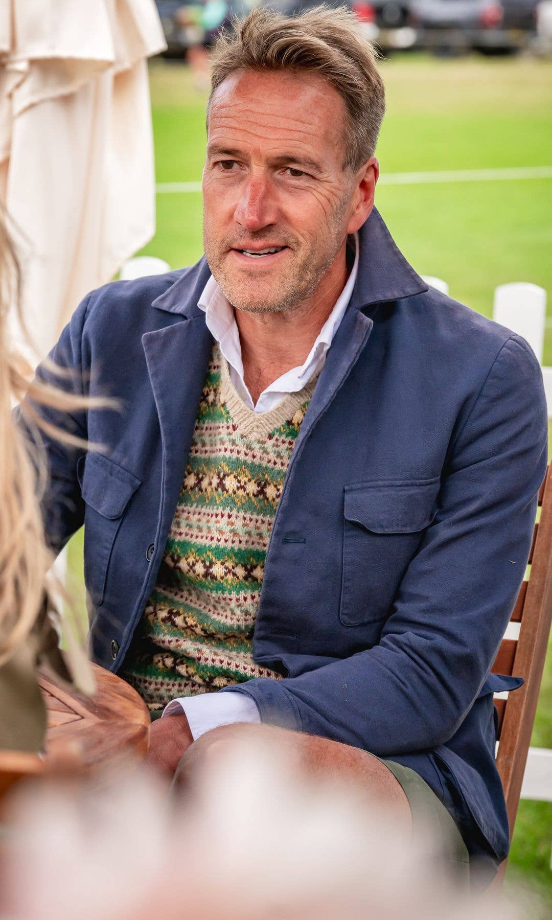 Ben Fogle sits at a table under a white umbrella, smiling at a woman.