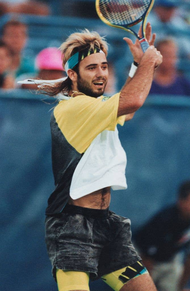 Andre Agassi playing tennis, wearing a yellow and gray shirt, black shorts, and a headband.
