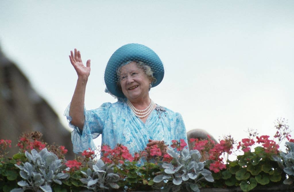 The Queen Mother waving in a blue outfit with a matching hat in 1987.