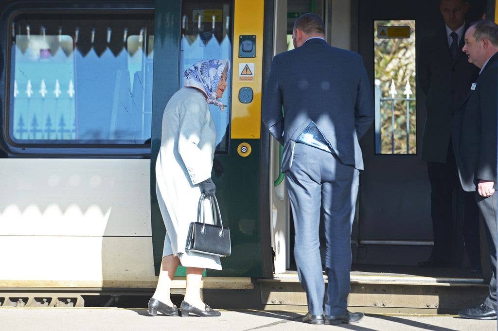 Queen Elizabeth II in white dress and headscarf boarding a train with an aide.