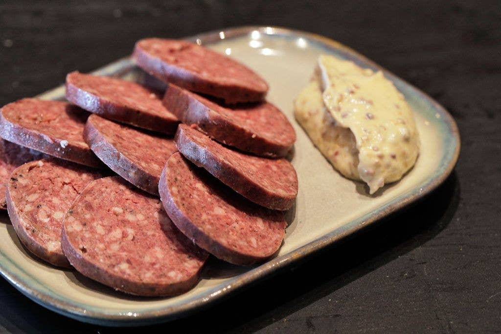 Sliced liverwurst arranged on a ceramic plate beside a dollop of grainy mustard.