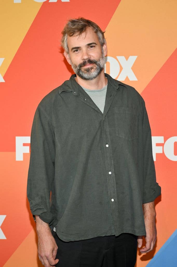 Rossif Sutherland smiles for photographers at the FOX Fall TV press junket, wearing an olive green shirt over a grey t-shirt.
