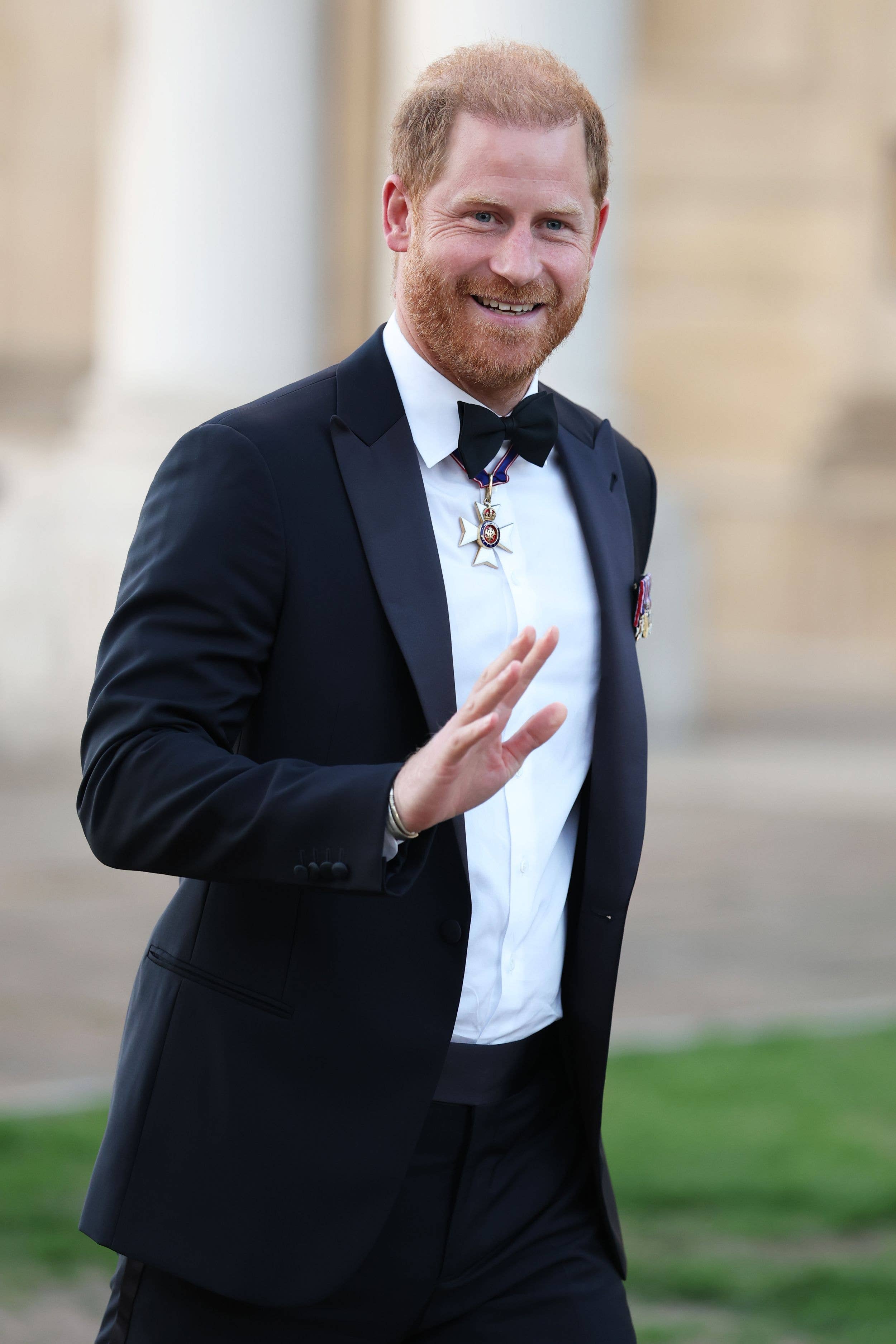 Prince Harry, Duke of Sussex, in a black tuxedo with medals, smiling and gesturing.