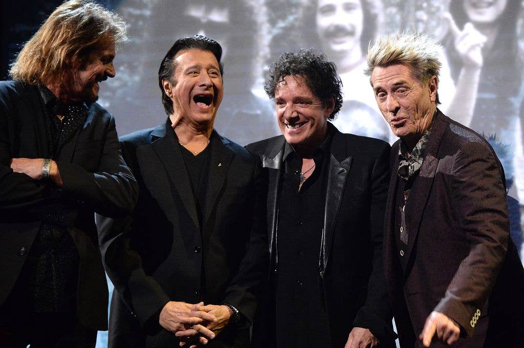 Neal Schon, Steve Perry, Ross Valory, and Gregg Rolie stand together, smiling and laughing on stage.