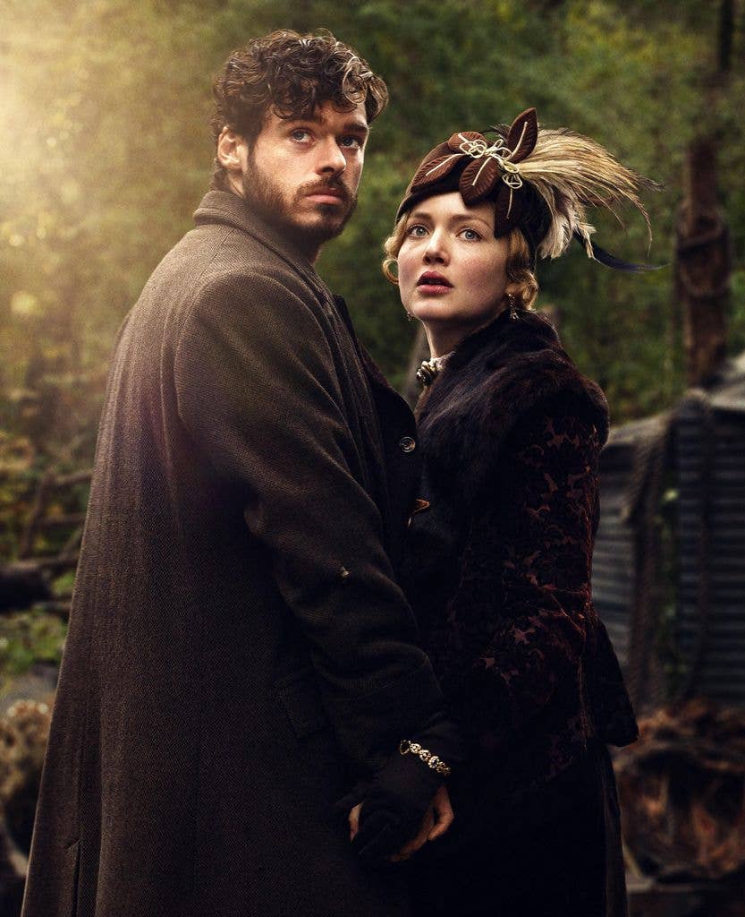 Richard Madden and Holliday Grainger standing close, dressed in vintage attire, in a forest setting.