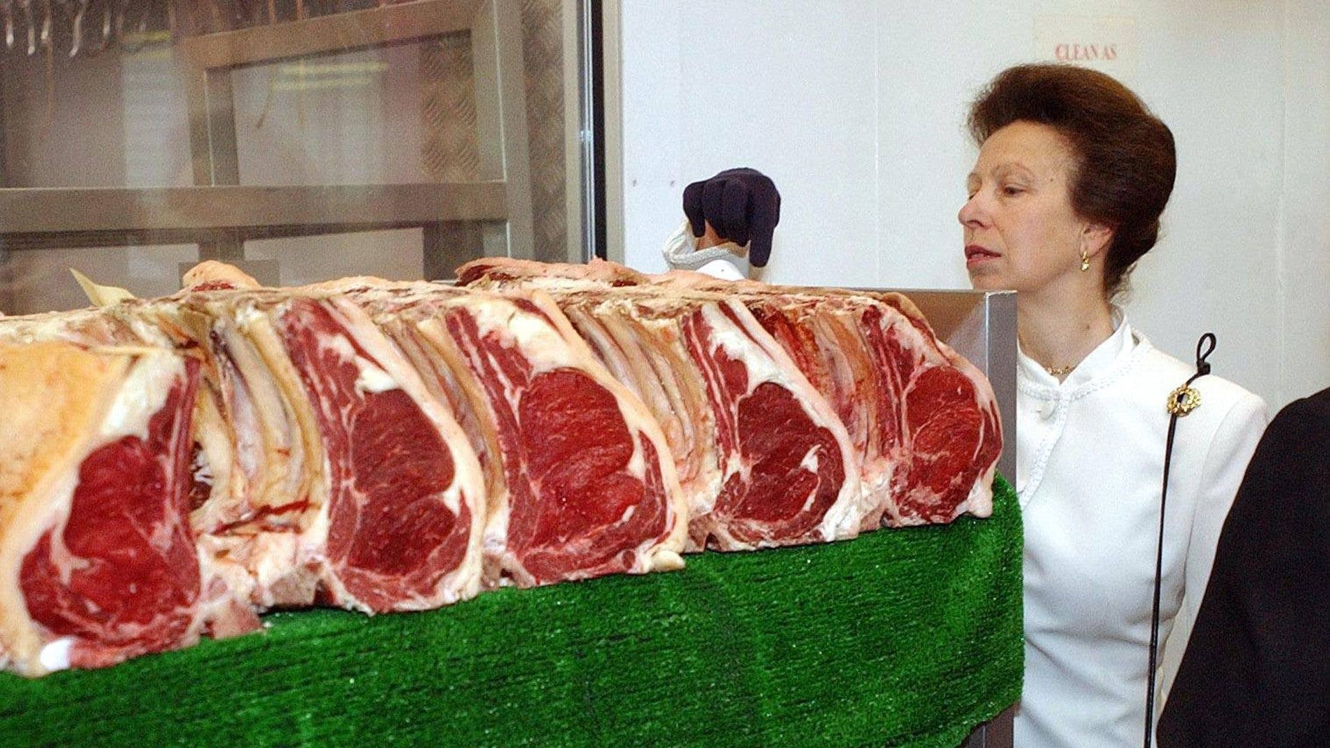 Anne, Princess Royal, in a white blouse, examines raw meat on a green surface.