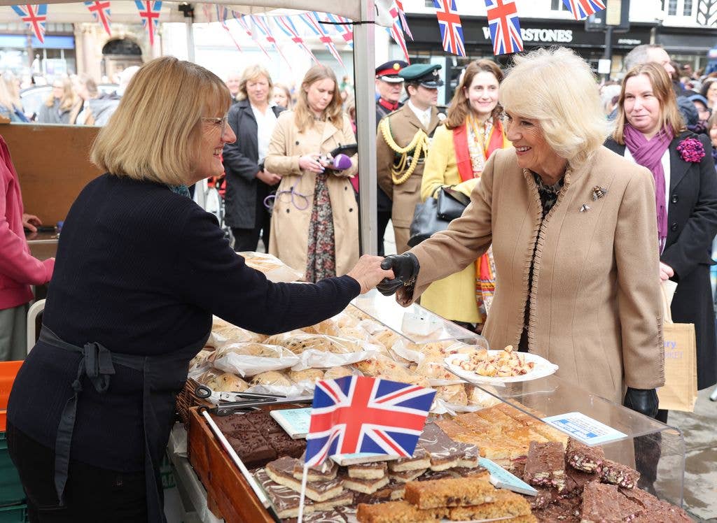 Queen Camilla smiles and shakes hands with a market trader during her visit to the Farmers' Market on March 27, 2024 in Shrewsbury, England.